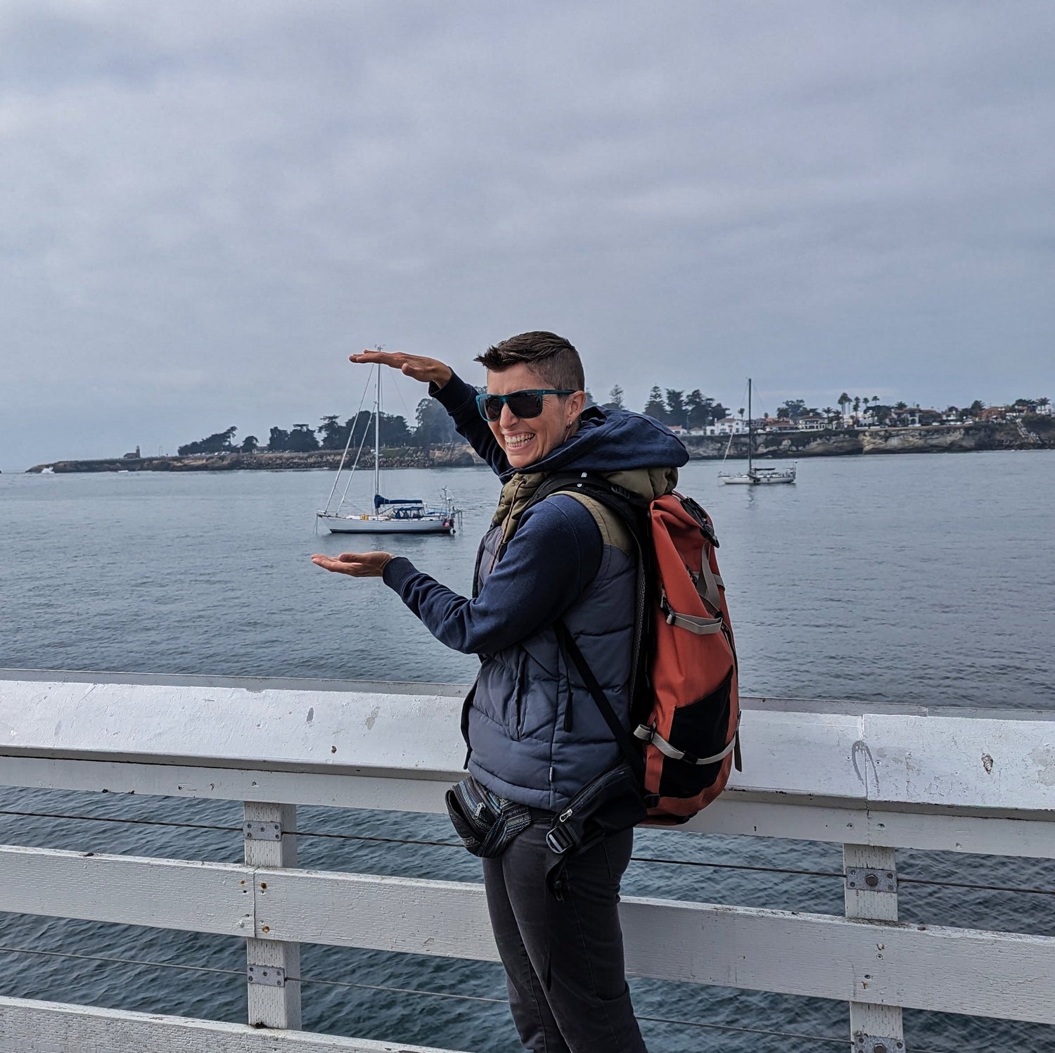 A person standing on a pier trying to look like they are holding a far off boat between their hands